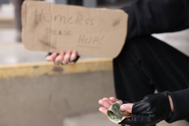 Tabela ve paralı evsiz bir adam, seçici bir odak.