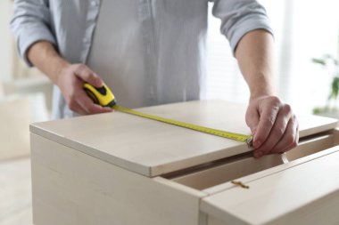 İçerideki bantla ahşap dolabı ölçen adam, yakın plan.