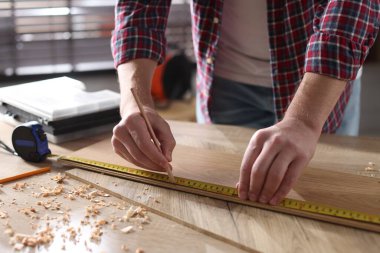 Kapalı alanda bant ile ahşap kalas ölçen bir adam.