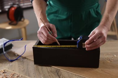 İçerideki ahşap masada bant ile ölçüm yapan adam, yakın plan.