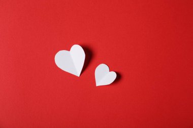 Kırmızı zemin üzerinde kağıt kalpler, düz uzanmış