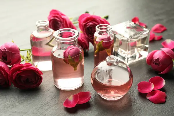 Gri desenli masa üzerinde aromatik esanslı yağlar ve güllerle parfüm şişelerini aç, yakın plan.