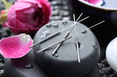 Akupunktur iğneleri, ıslak spa taşları ve hasır hasırın üzerindeki çiçekler, yakın plan.