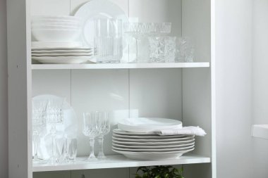 Beyaz duvarın yanındaki raflarda temiz bardaklar ve tabaklar.