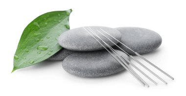 Akupunktur iğneleri, spa taşları ve yaprakları beyaza izole edilmiş.