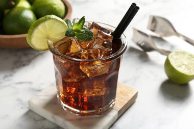 Lezzetli Küba Libre kokteyli, beyaz mermer masada limon ve maşa, yakın plan.