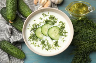 Lezzetli salatalık çorbası kasede ve açık mavi ahşap masada malzemeler.