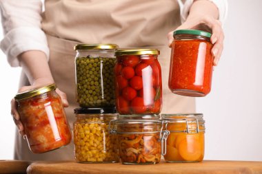 Farklı turşulu ürünlerle dolu kavanozları olan kadın arka planda ışığa karşı, yakın plan.