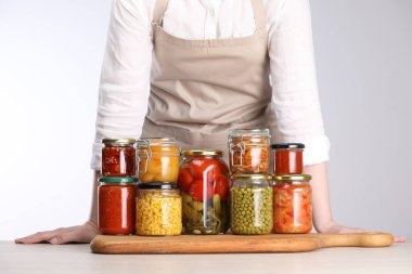 Açık gri arka planda farklı turşulu ürünlerle dolu kavanozları olan kadın, yakın plan.