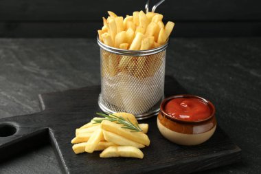 Lezzetli patates kızartması, ketçap ve biberiye ile servis ediliyor, siyah masada, yakın plan.