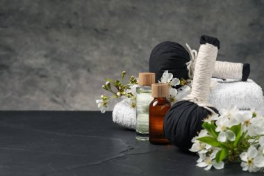 Kozmetik ürünleri ve güzel çiçeklerle kaplıca kompozisyonu siyah desenli tablo üzerinde gri arkaplan, metin için boşluk