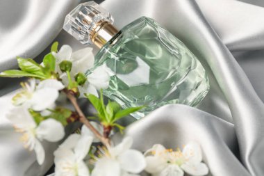 Bir şişe aromatik parfüm ve güzel çiçekli gri ipek kumaş, yakın plan.