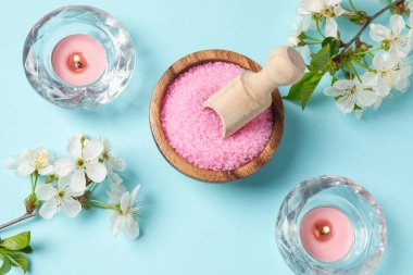 Deniz tuzu, yanan mumlar ve açık mavi arka planda güzel çiçekler içeren spa kompozisyonu.