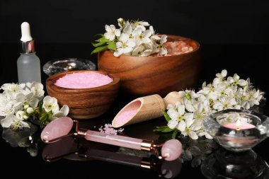 Siyah ayna yüzeyinde kozmetik ürünleri ve güzel çiçeklerle kaplıca kompozisyonu, yakın plan.