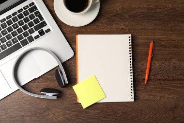 Not defteri, yapışkan not, kalem, kulaklık, kahve ve dizüstü bilgisayar ahşap masaya, düz uzan.
