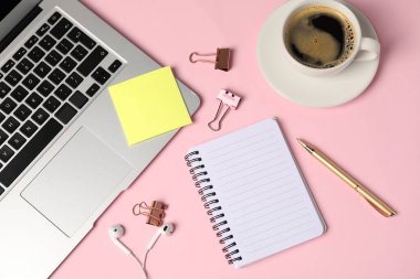Not defteri, yapışkan not, kalem, cilt klipleri, kahve, kulaklık ve pembe arka planda dizüstü bilgisayar, düz yatış