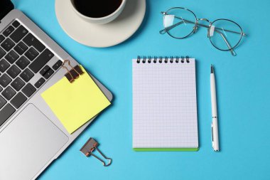 Not defteri, yapışkan not, kalem, cilt klipsi, açık mavi zemin üzerinde kahve ve dizüstü bilgisayar, düz uzanma