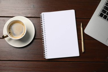 Defter, kalem, kahve ve dizüstü bilgisayar ahşap masada, düz yatıyordu.