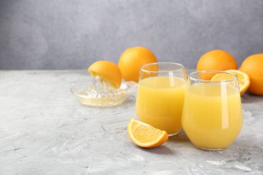 Bardakta portakal suyu, gri masada taze meyve suyu ve meyve sıkacağı, mesaj için yer.