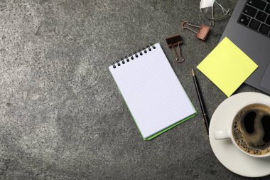 Not defteri, kalem, yapışkan not, kahve, cilt klipsleri, ve gri masadaki dizüstü bilgisayar, düz. Metin için boşluk