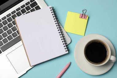 Not defteri, yapışkan not, kalem, kahve ve dizüstü bilgisayar açık mavi arka planda, düz uzanış