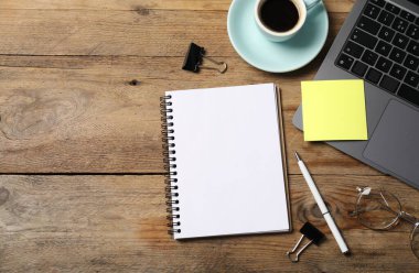 Kalemli defter, yapışkan not, dizüstü bilgisayar, ataç ve tahta sehpada kahve. Metin için boşluk