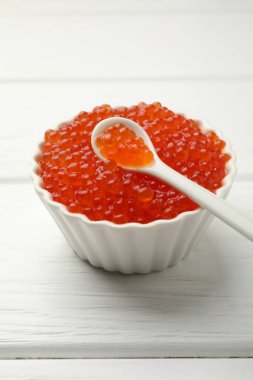 Lezzetli kırmızı havyar kasede ve kaşık beyaz ahşap masada, yakın plan