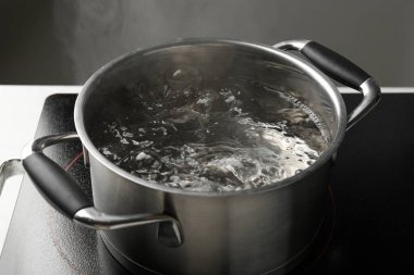 Kaynar suyla pişirme tenceresi ve beyaz masa üzerinde gri arka plan, yakın çekim
