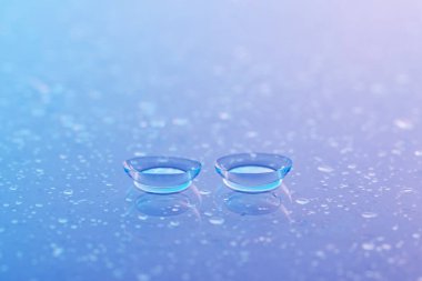 Bir çift kontakt lens ve su damlası mor ayna yüzeyine düşer, yakın plan.
