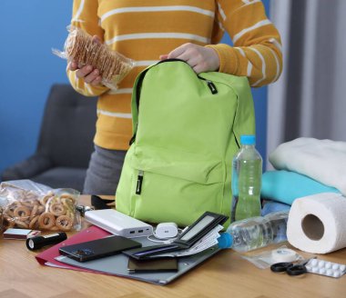 Hayatta kalma kiti. Kadın, ahşap masada sırt çantasına farklı acil durum malzemeleri yerleştiriyor.