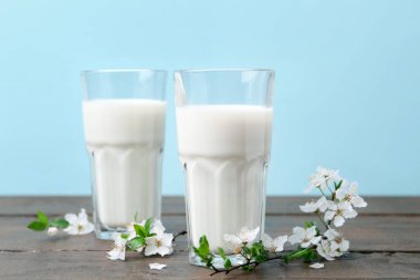 Taze süt ve çiçekler beyaz masada açık mavi arka planda