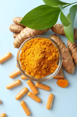 Açık mavi zemin üzerinde zerdeçal kapsülleri, toz, kökler ve yeşil yapraklar düz uzanır