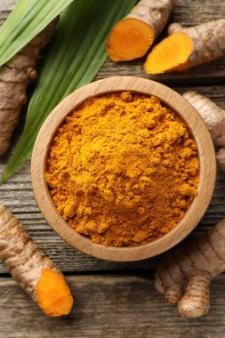 Tabaktaki zerdeçal tozu, kökler ve yapraklar ahşap masada, düz yerde.