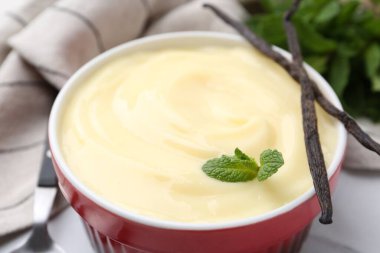Tasty vanilla pudding, mint and pods on white table, closeup