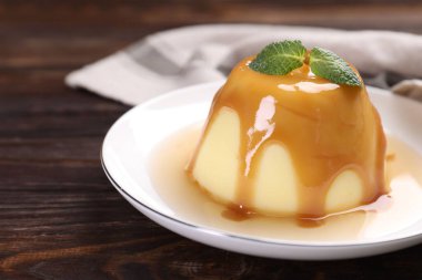Karamel soslu lezzetli puding ve ahşap masada nane şekeri, yakın plan.
