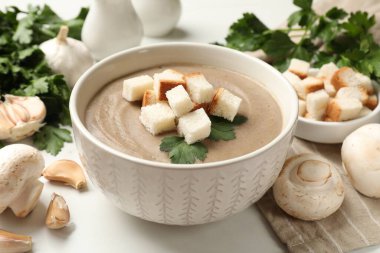 Ekmek arası mantar kremalı çorba, maydanoz ve malzemeler ışık masasında.