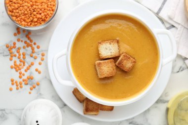 Lezzetli mercimek kremalı çorba, beyaz mermer masa üzerinde kızarmış ekmeklerle servis edilir.