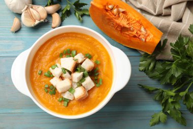 Ekmek arası balkabağı kremalı çorba, yeşil soğan, sarımsak ve maydanoz açık mavi ahşap masa, düz uzanmış