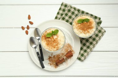 Tarçınlı, nane, badem ve kaşıklı lezzetli sütlaç beyaz ahşap masa, düz uzanmış