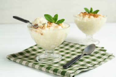 Tarçınlı lezzetli sütlaç, nane ve kaşıklar beyaz ahşap masada, yakın plan.