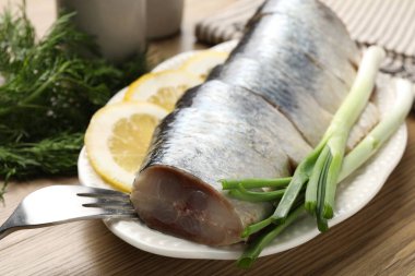 Limon dilimli lezzetli ringa balıkları, yeşil soğan ve ahşap masada dereotu, yakın plan.