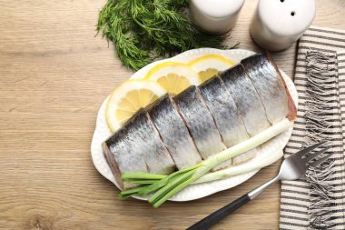 Limon dilimli lezzetli ringa balıkları, yeşil soğan ve ahşap masa üzerinde dereotlar.