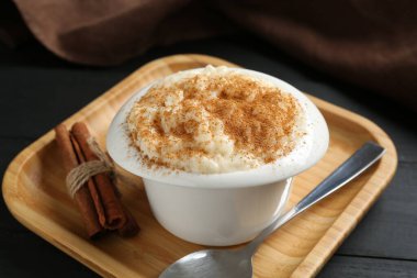 Tarçınlı lezzetli sütlaç ve siyah ahşap masada kaşık, yakın plan.