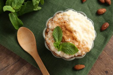 Tarçınlı, naneli, bademli ve tahta masadaki kaşıklı lezzetli sütlaç.