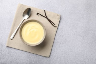 Lezzetli vanilyalı puding kasede, kapsüller ve kaşık açık gri masada, düz yerde. Metin için boşluk