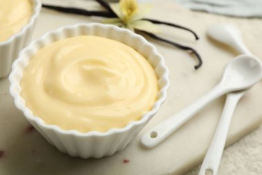 Kaşıklar, kapsüller ve çiçekli lezzetli vanilyalı puding açık dokulu masa, yakın çekim.
