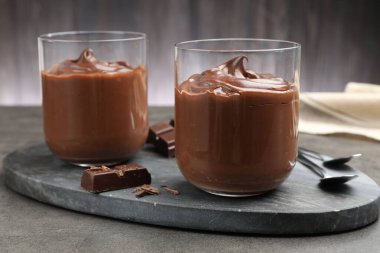 Lezzetli puding ve çikolata parçaları gri masada, yakın plan.