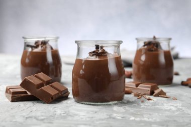 Cam kavanozlarda lezzetli puding ve açık gri masada çikolata parçaları, yakın plan.