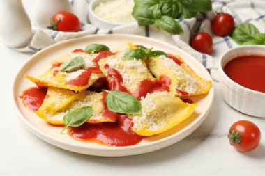 Domates soslu lezzetli ravioli, parmesan peyniri ve fesleğen beyaz masada, yakın plan.