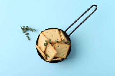 Açık mavi arka planda leziz tuzlu krakerler ve kekik, üst manzara.